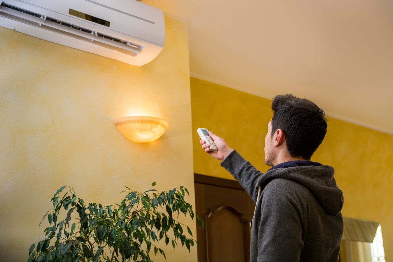 A young man operating an air conditioner with a remote.