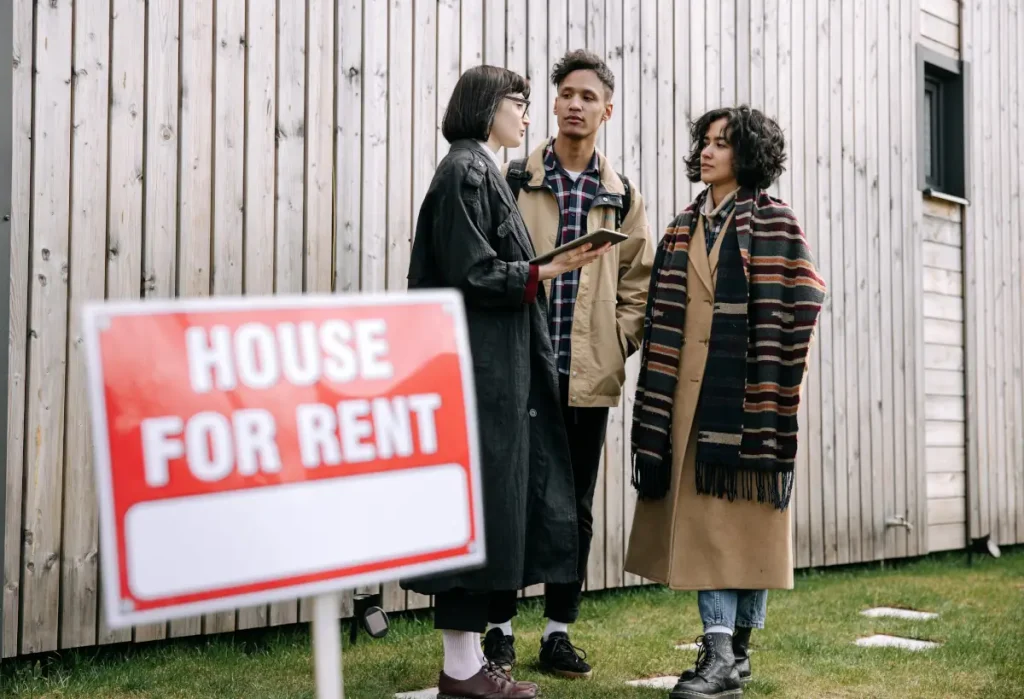 People talking beside a house rental sign